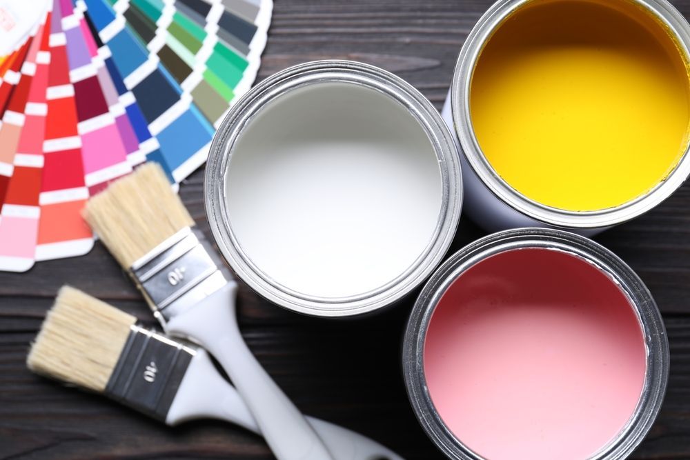 Paint cans with white, yellow, and pink paint beside brushes and color swatches