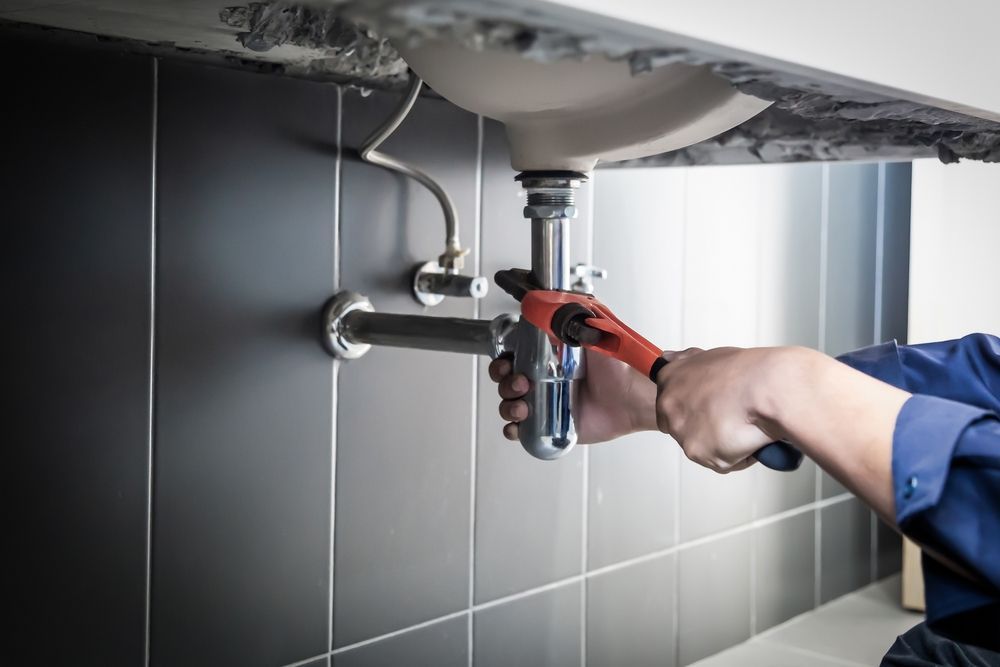Plumber using a wrench to repair a bathroom sink pipe under the counter