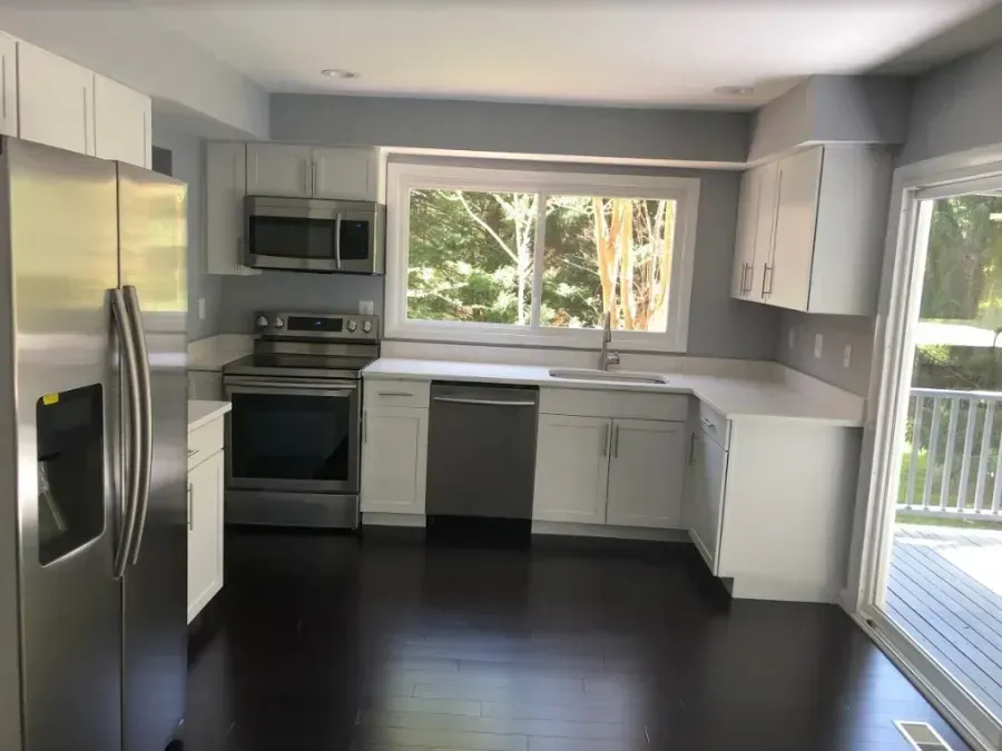 Bright kitchen with stainless steel appliances, white cabinets, dark floors, and a large window.
