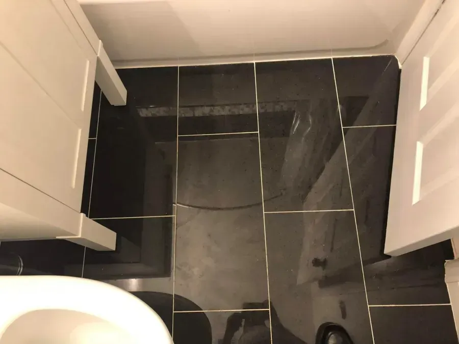 Black tiled bathroom floor beside white cabinets, with a toilet partially visible in the corner.