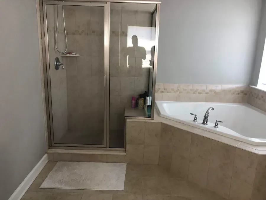 Bathroom with glass shower, beige tile, white tub, and light gray walls
