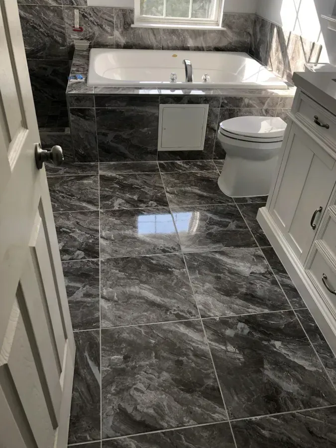 Modern bathroom with black marble tile, white vanity, bathtub, and toilet