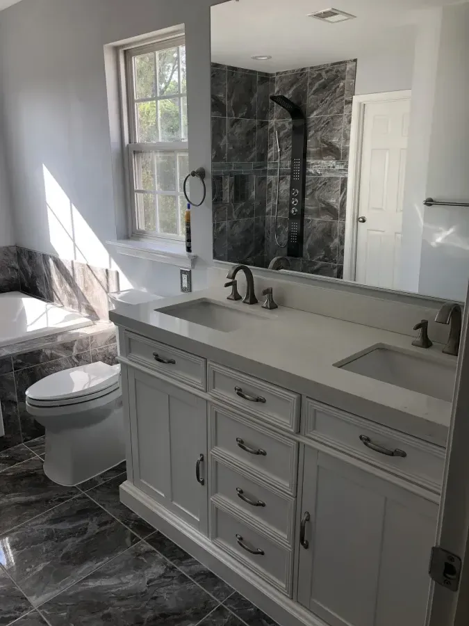 Modern bathroom with double vanity, dark marble floor, glass shower, and sunlight from a window