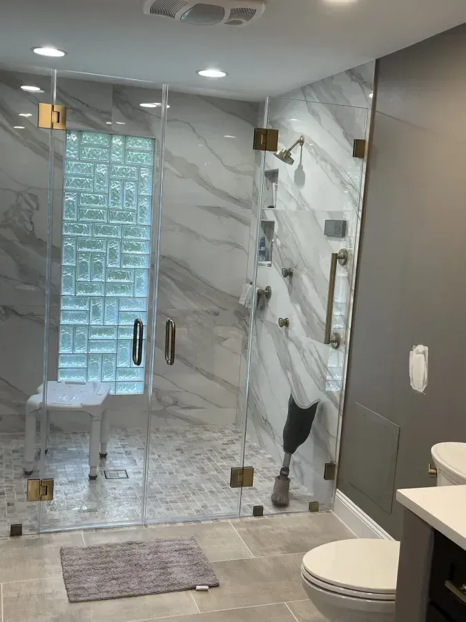 Modern bathroom with glass shower, marble tile, gray floor, and toilet sink visible