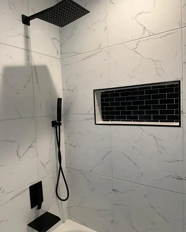 Modern shower with black square rainfall head, handheld sprayer, and black subway-tile niche on white marble walls