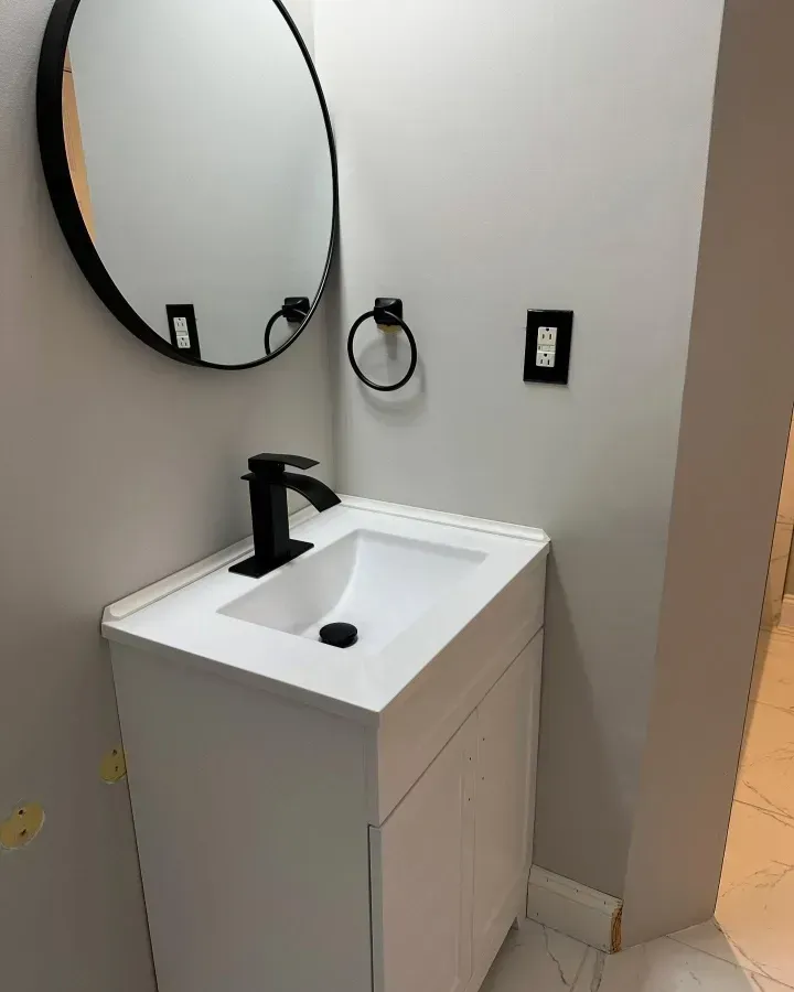 Small modern bathroom vanity with round mirror, white sink, and black faucet against light walls
