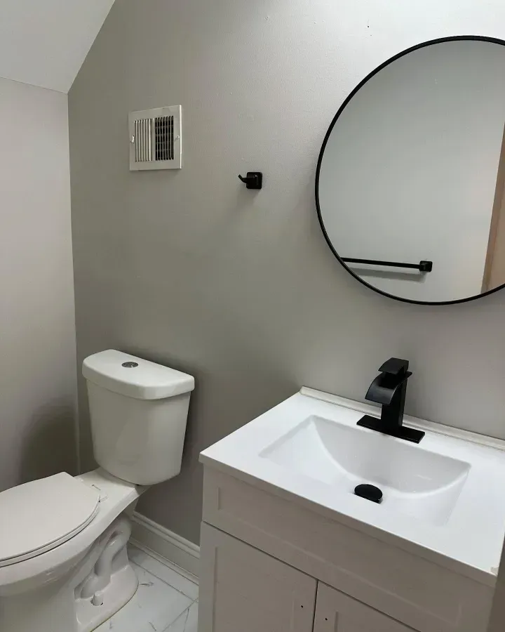 Small modern bathroom with toilet, vanity sink, round mirror, and light gray walls