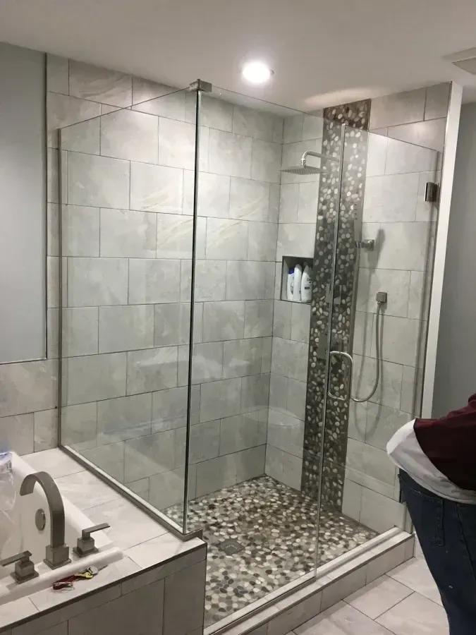 Glass walk-in shower with gray tile and pebble floor in a modern bathroom