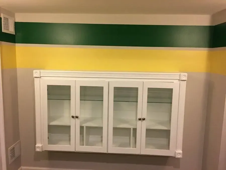 White glass-front wall cabinet beneath green, yellow, and white horizontal wall stripes.