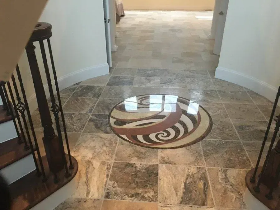Curved tiled hallway with a circular decorative medallion in the floor and stair railings on both sides