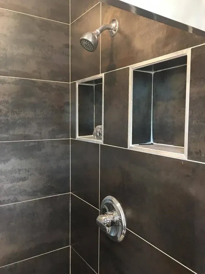 Bathroom shower with dark tile, chrome fixtures, and two recessed shelves
