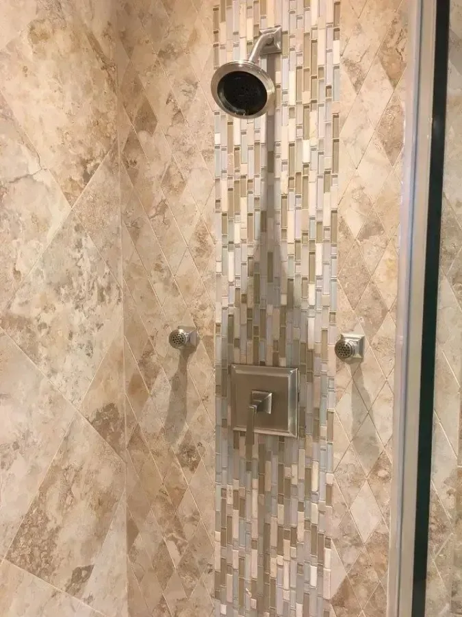 Modern shower with chrome fixtures, mosaic tile accent wall, and beige stone-patterned tiles.