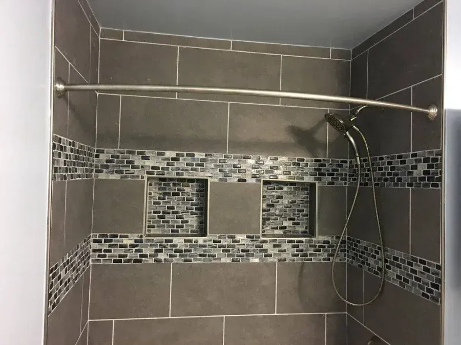 Modern tiled shower with gray walls, mosaic accent bands, and a handheld showerhead