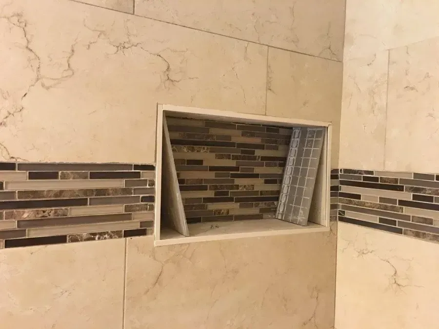Bathroom wall niche with beige marble tile and a dark mosaic accent border