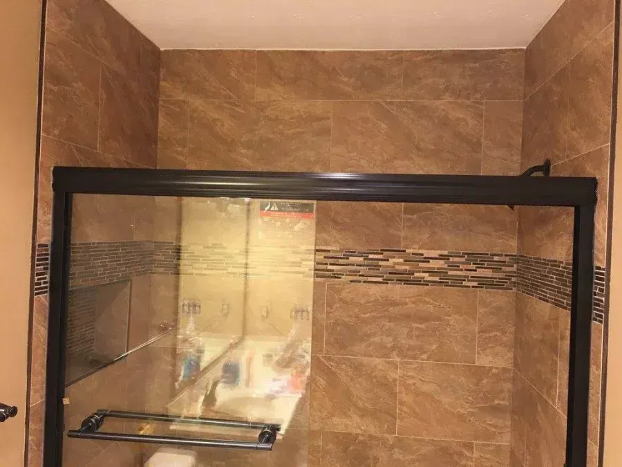 Bathroom shower stall with tan tile walls and a glass shower door.