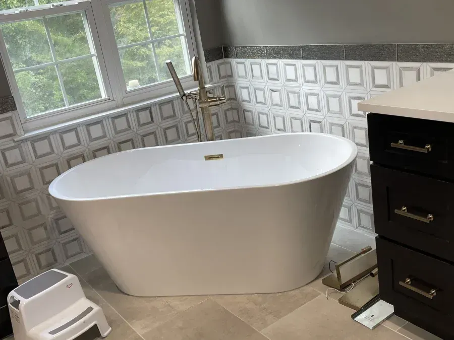 Modern bathroom with freestanding white tub, black vanity, tiled walls, window, and step stool
