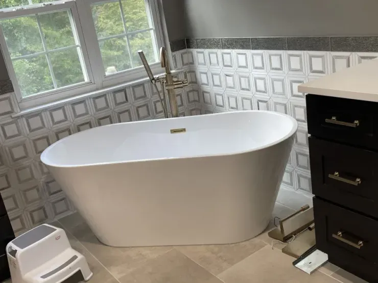 Modern bathroom with freestanding white tub, black vanity, tiled walls, window, and step stool