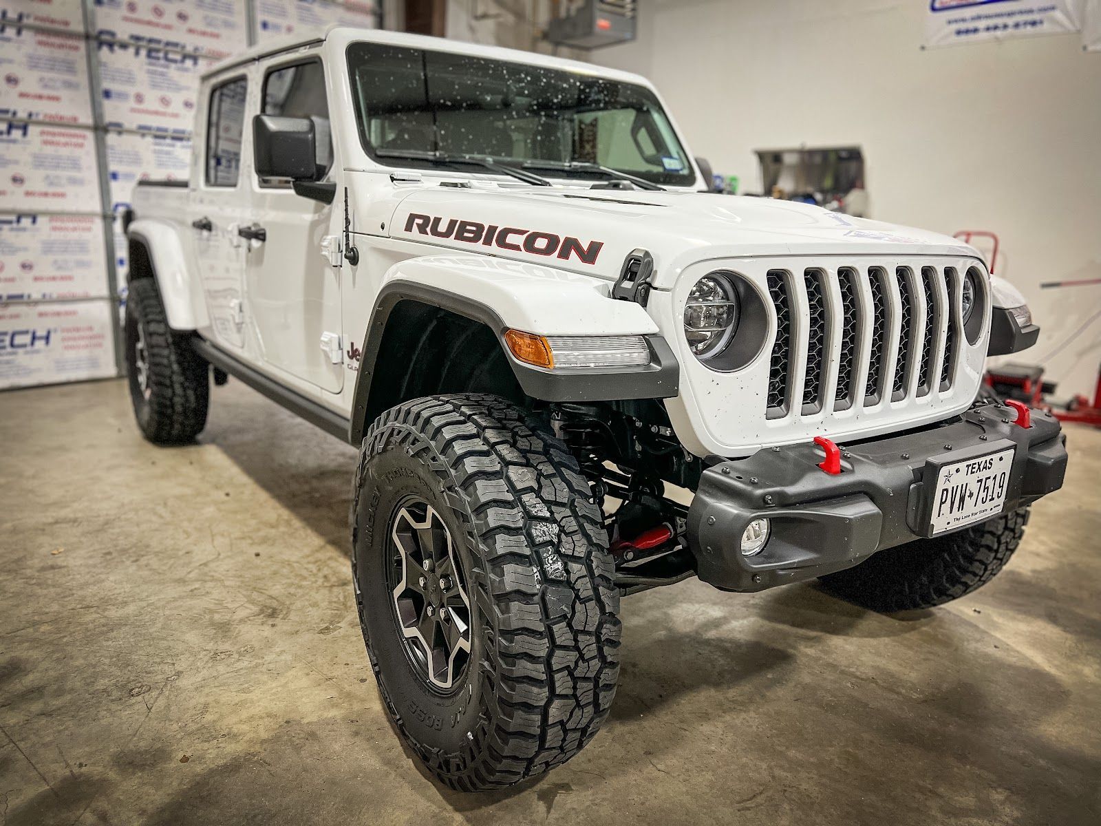 White Jeep Gladiator Rubicon pickup truck with large off-road tires, parked indoors. The truck is front-facing with 