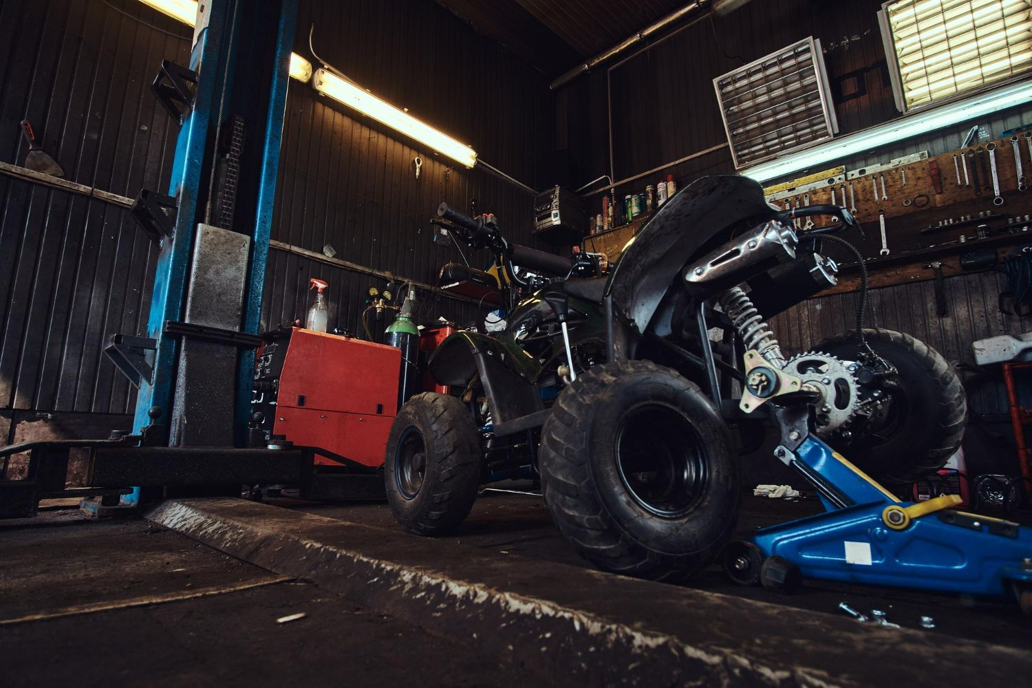 An ATV sits in a garage, raised by a jack. The dark setting suggests a repair.