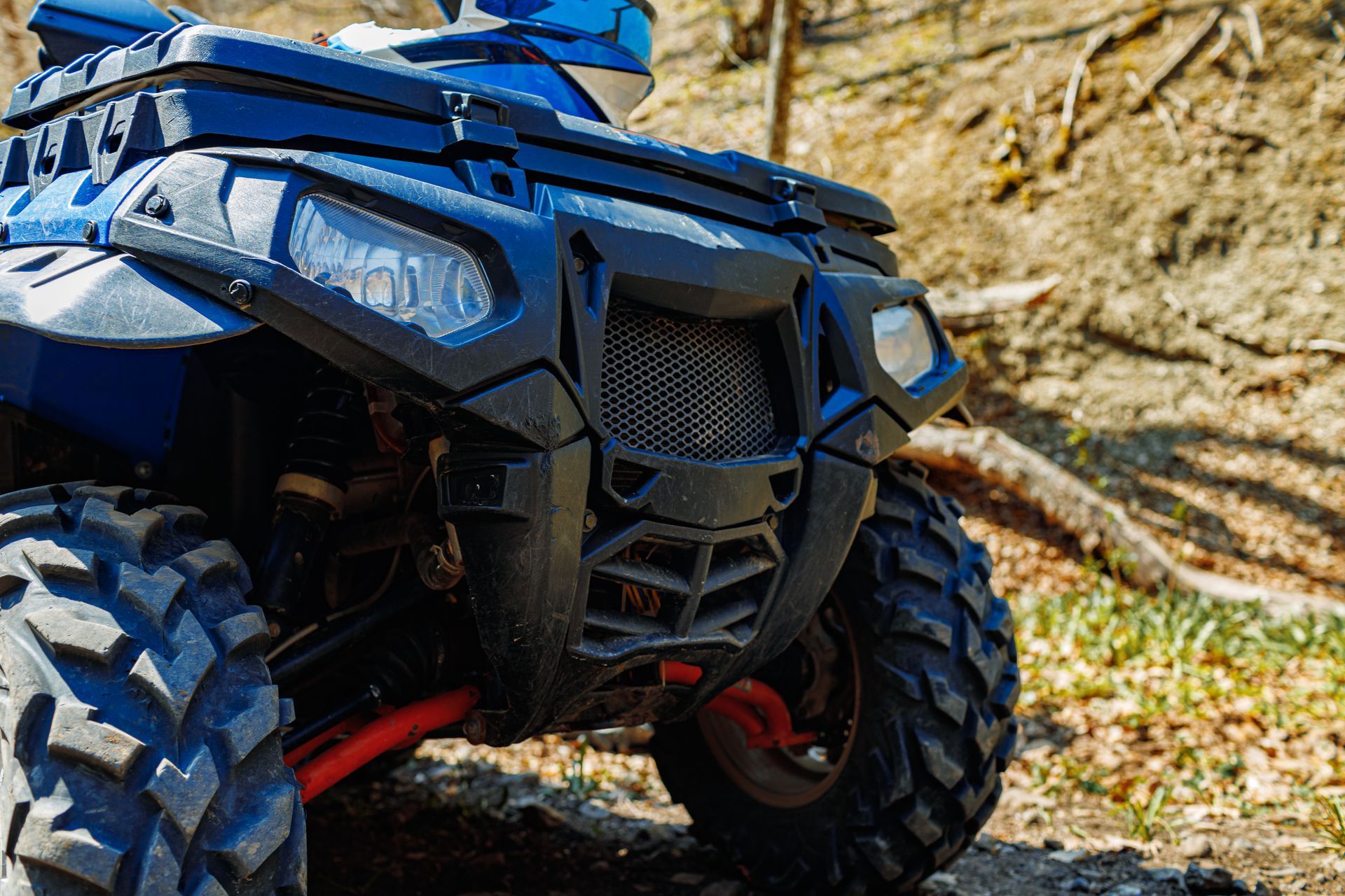 A blue atv is parked on a dirt road in the woods.