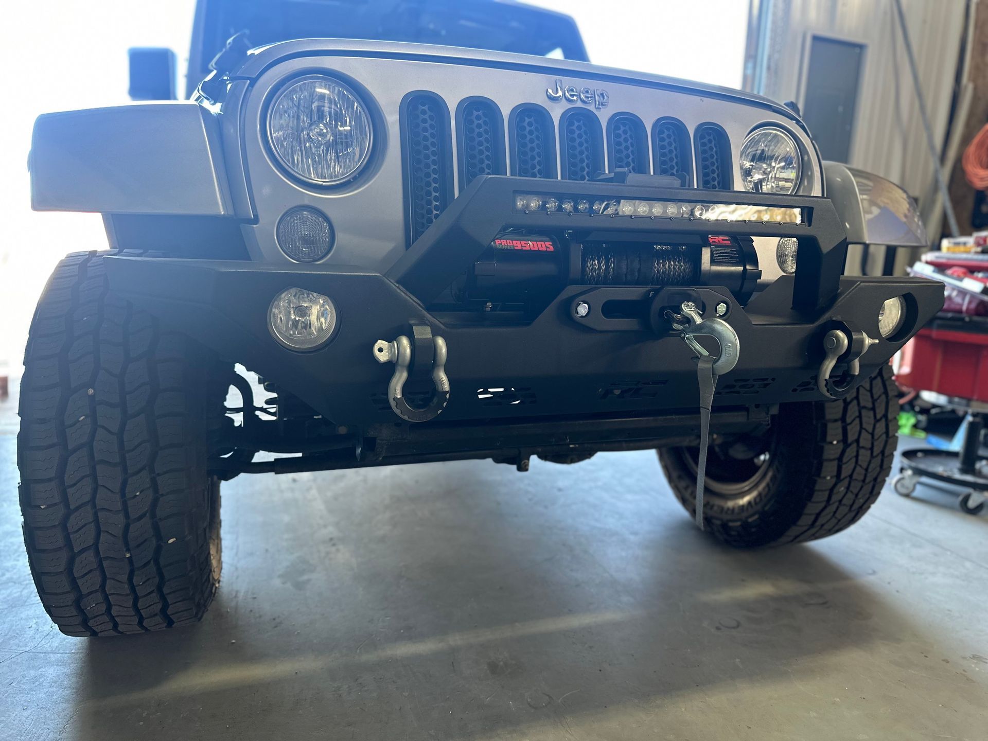 Gray Jeep Wrangler with black off-road bumper, winch, and light bar, parked indoors.
