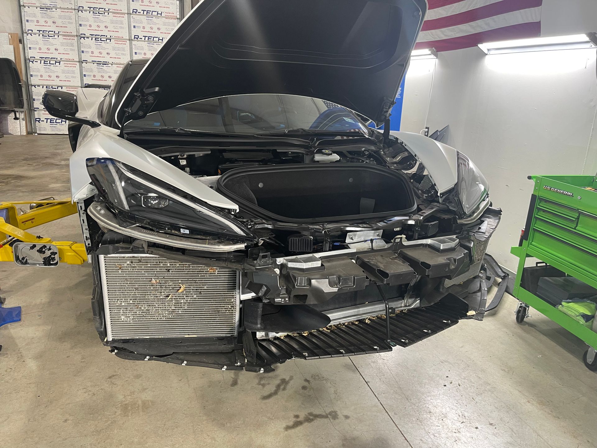 A car with the hood open is sitting on a lift in a garage.