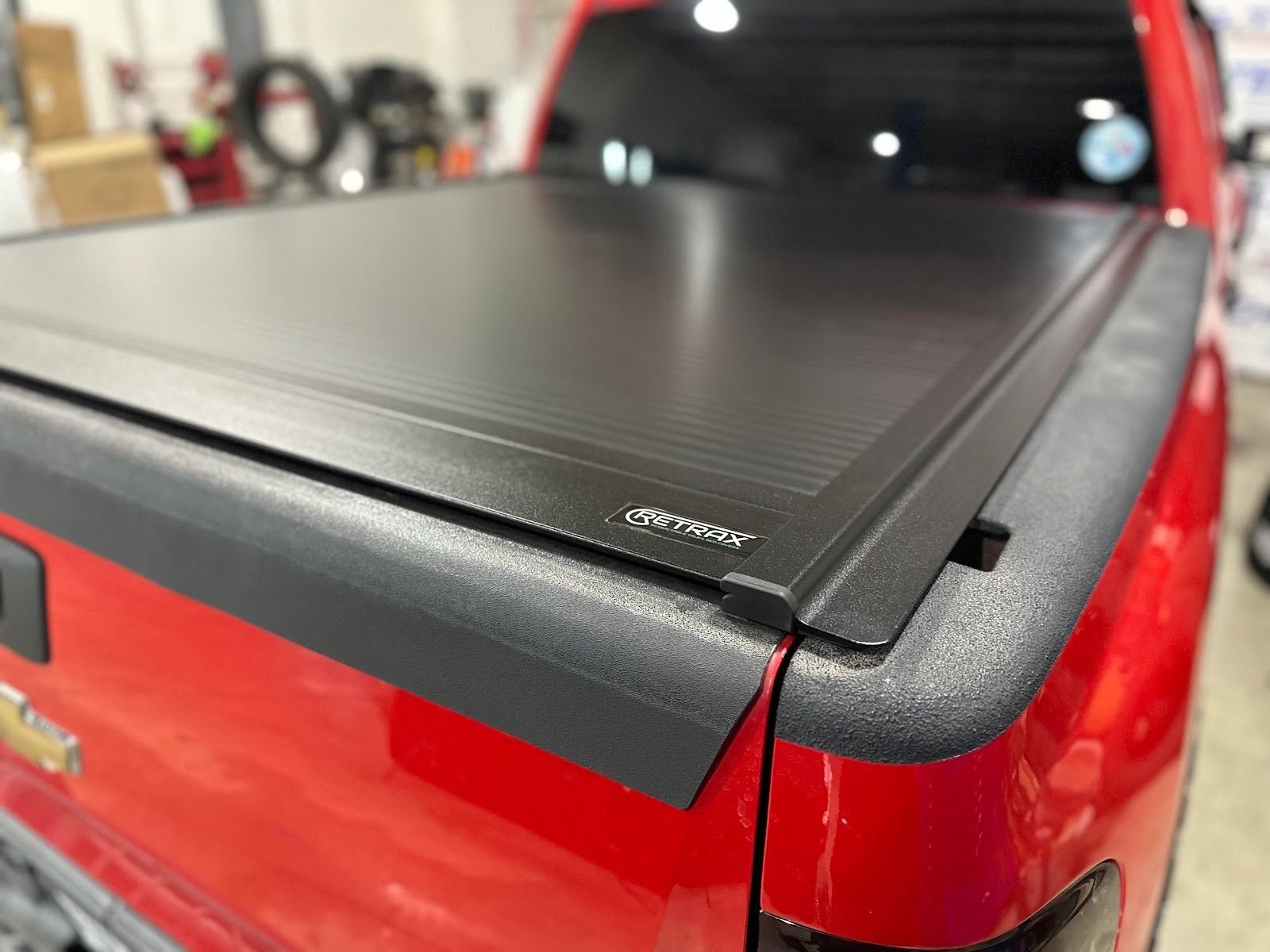 Red pickup truck bed with a black, retractable tonneau cover. The cover is closed and has a textured surface.