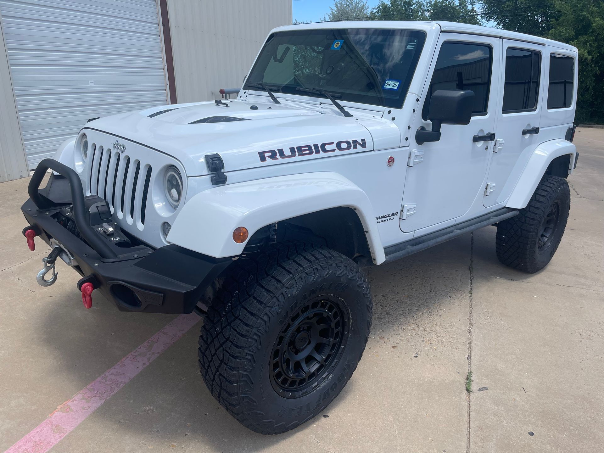 White Jeep Rubicon with black wheels and accents parked outside a building.
