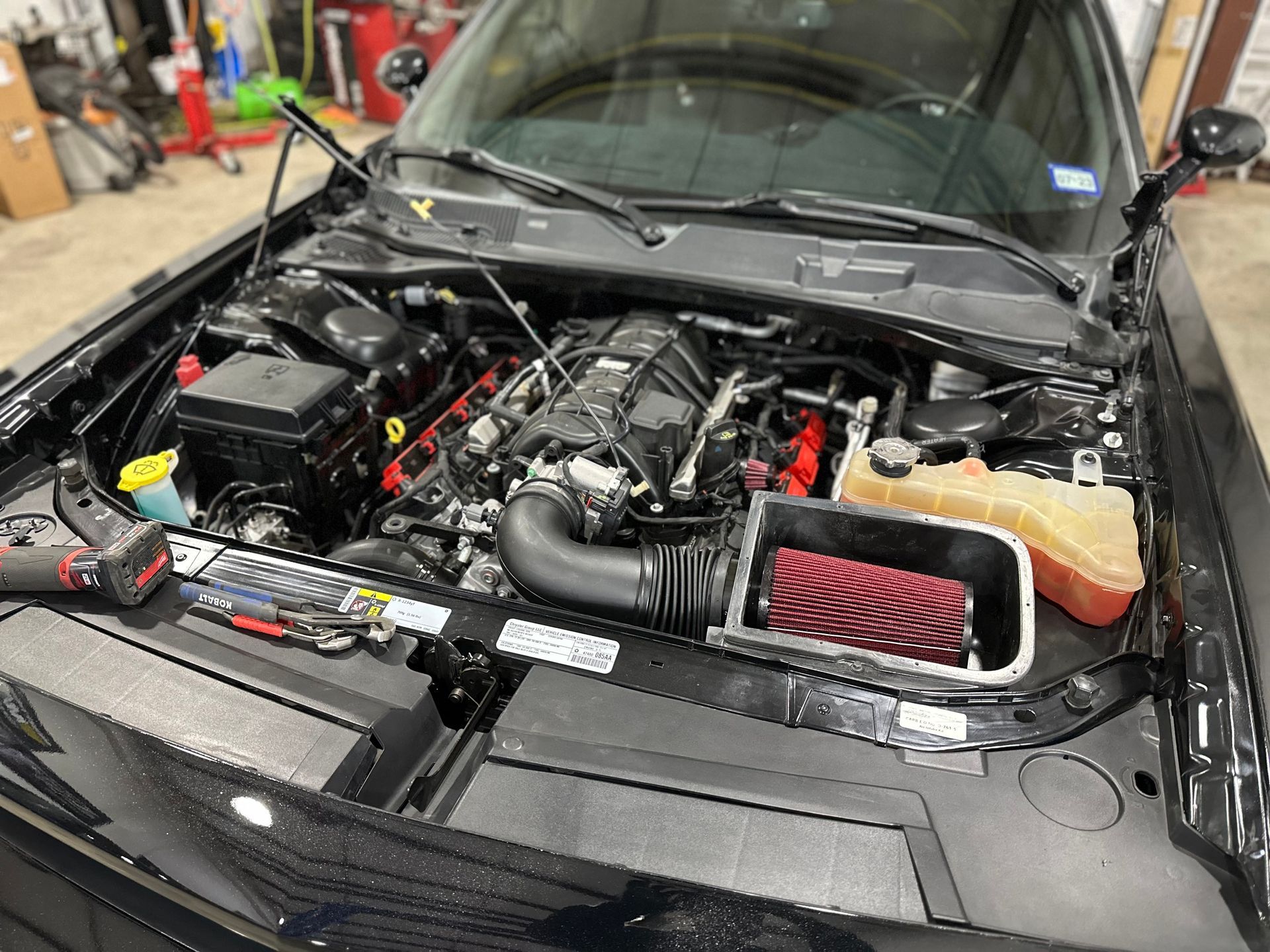 the engine of a black dodge challenger is shown with the hood open .