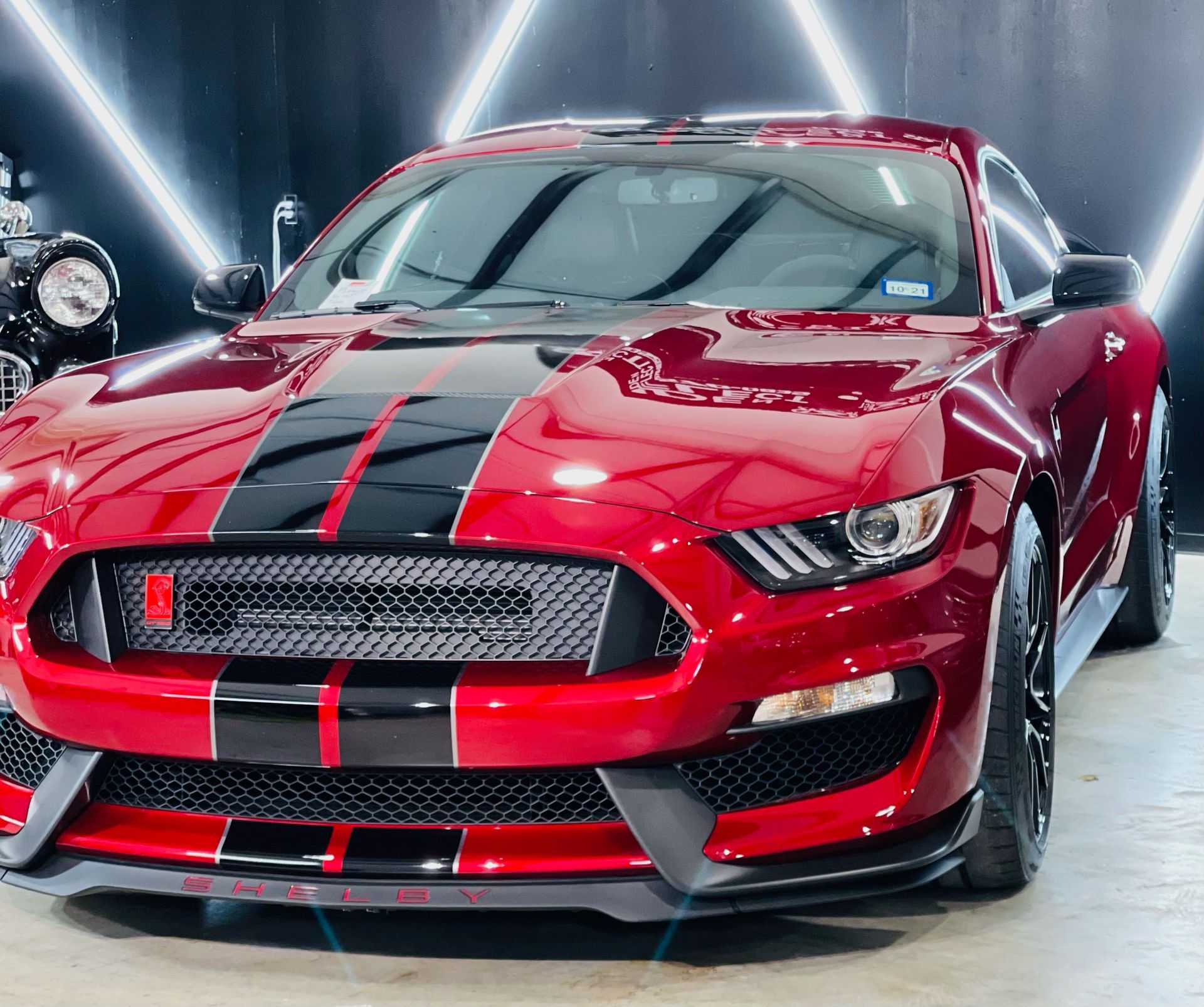 a red mustang with black stripes is parked in a garage .
