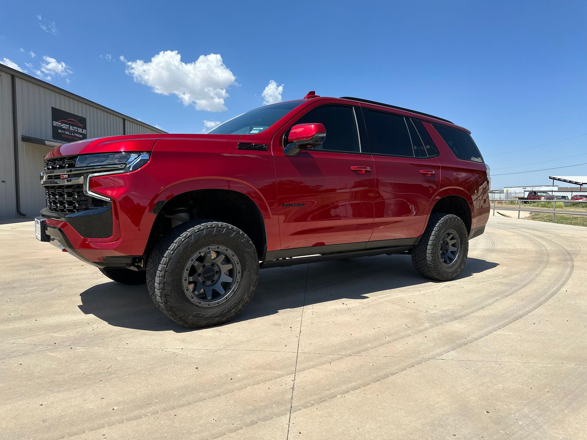 a red suv is parked on a dirt road in front of a building .