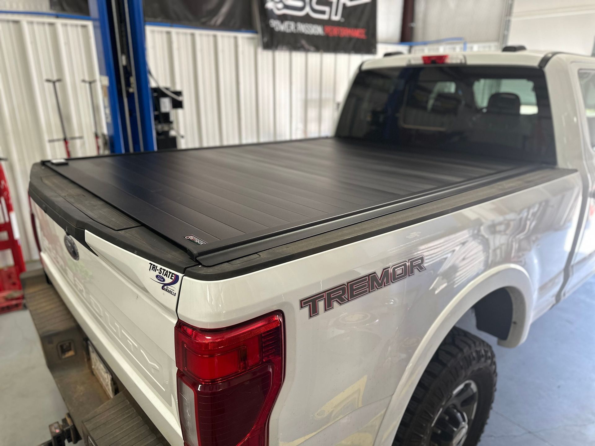 a white truck with a black bed cover is parked in a garage .