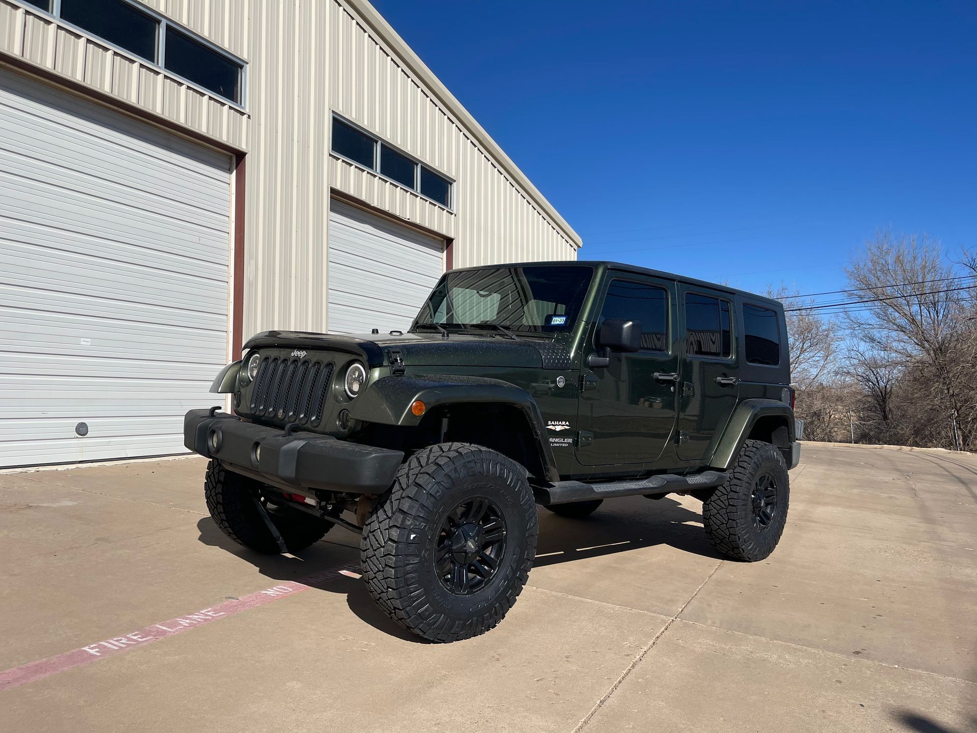a green jeep is parked in front of a garage door .