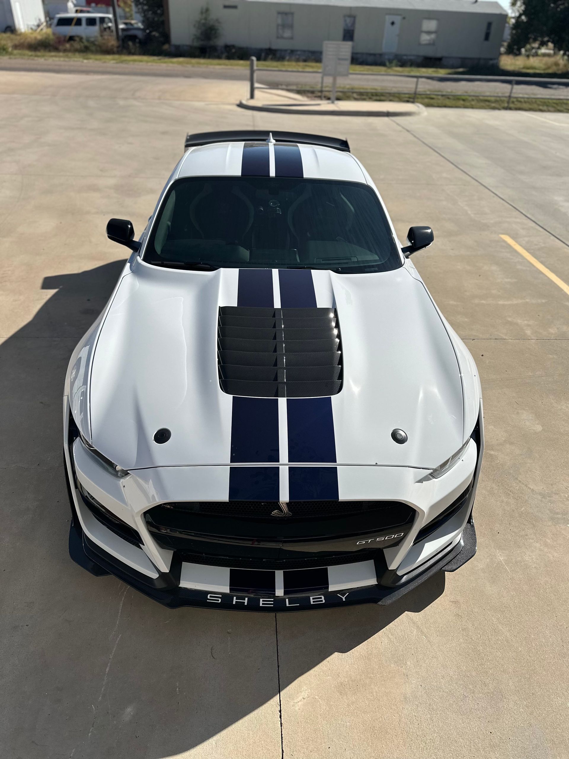 a white mustang with blue stripes on the hood is parked in a parking lot .