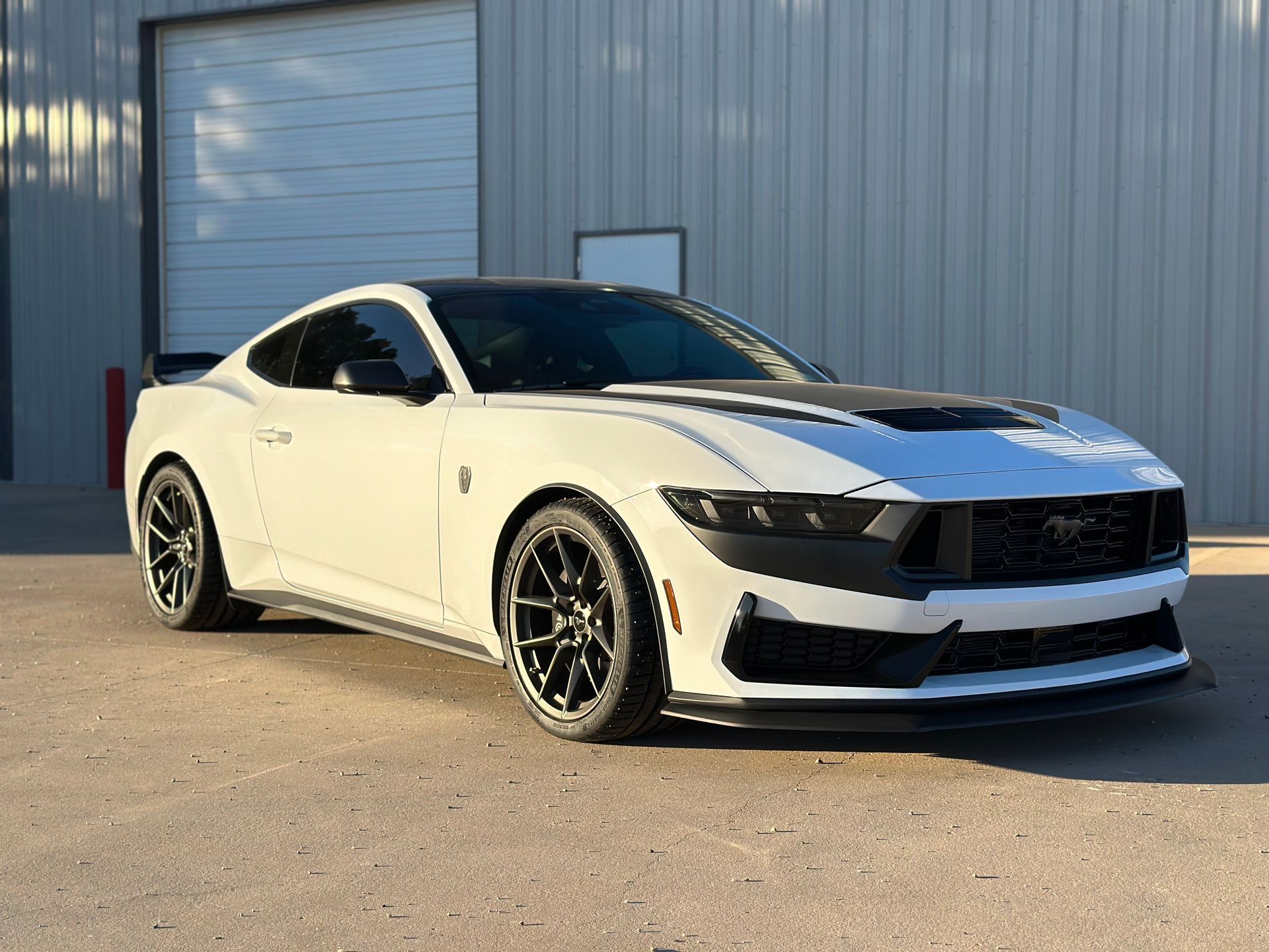 a white mustang is parked in front of a garage door .