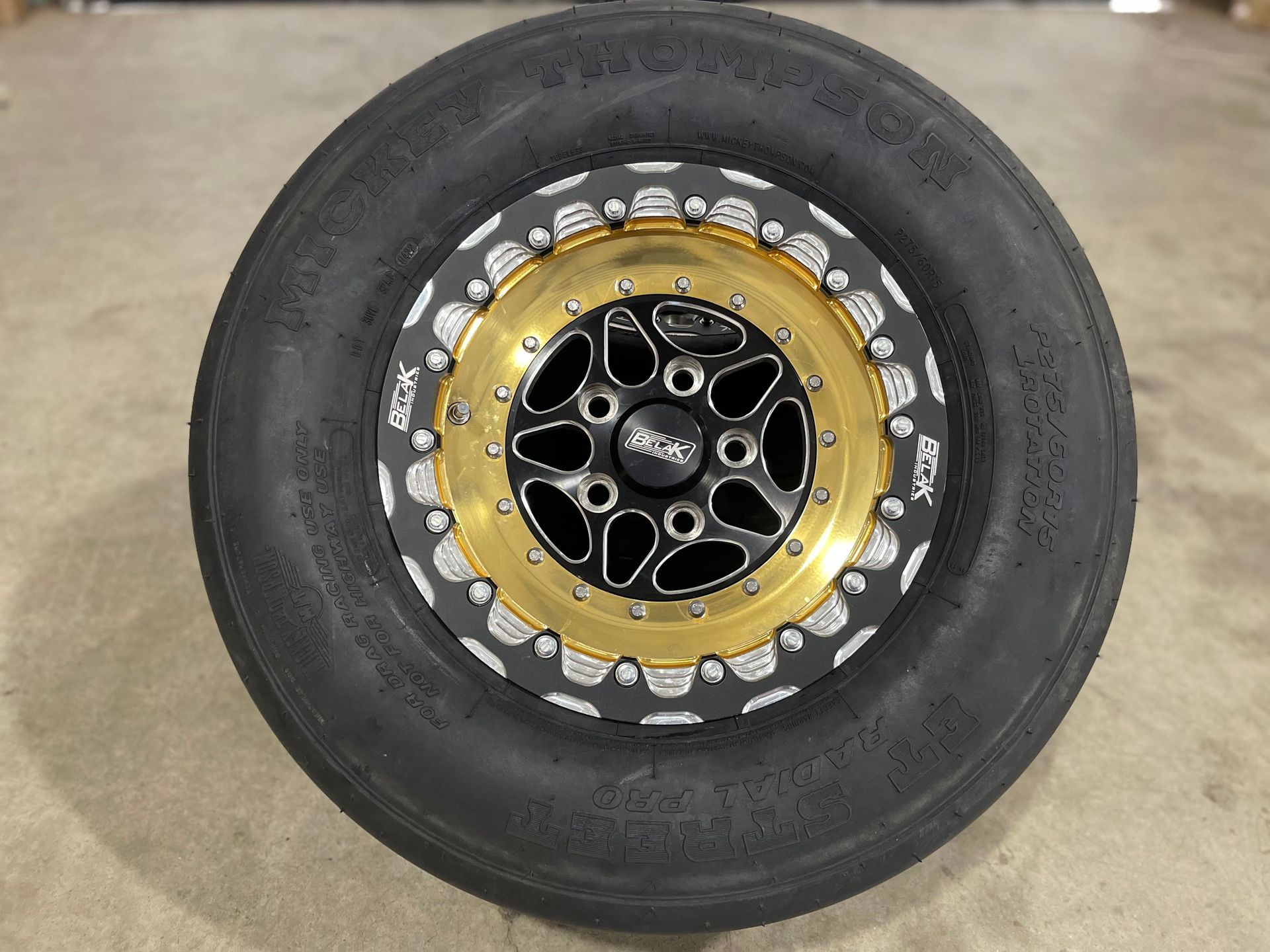 a black tire with a gold rim is sitting on the ground .