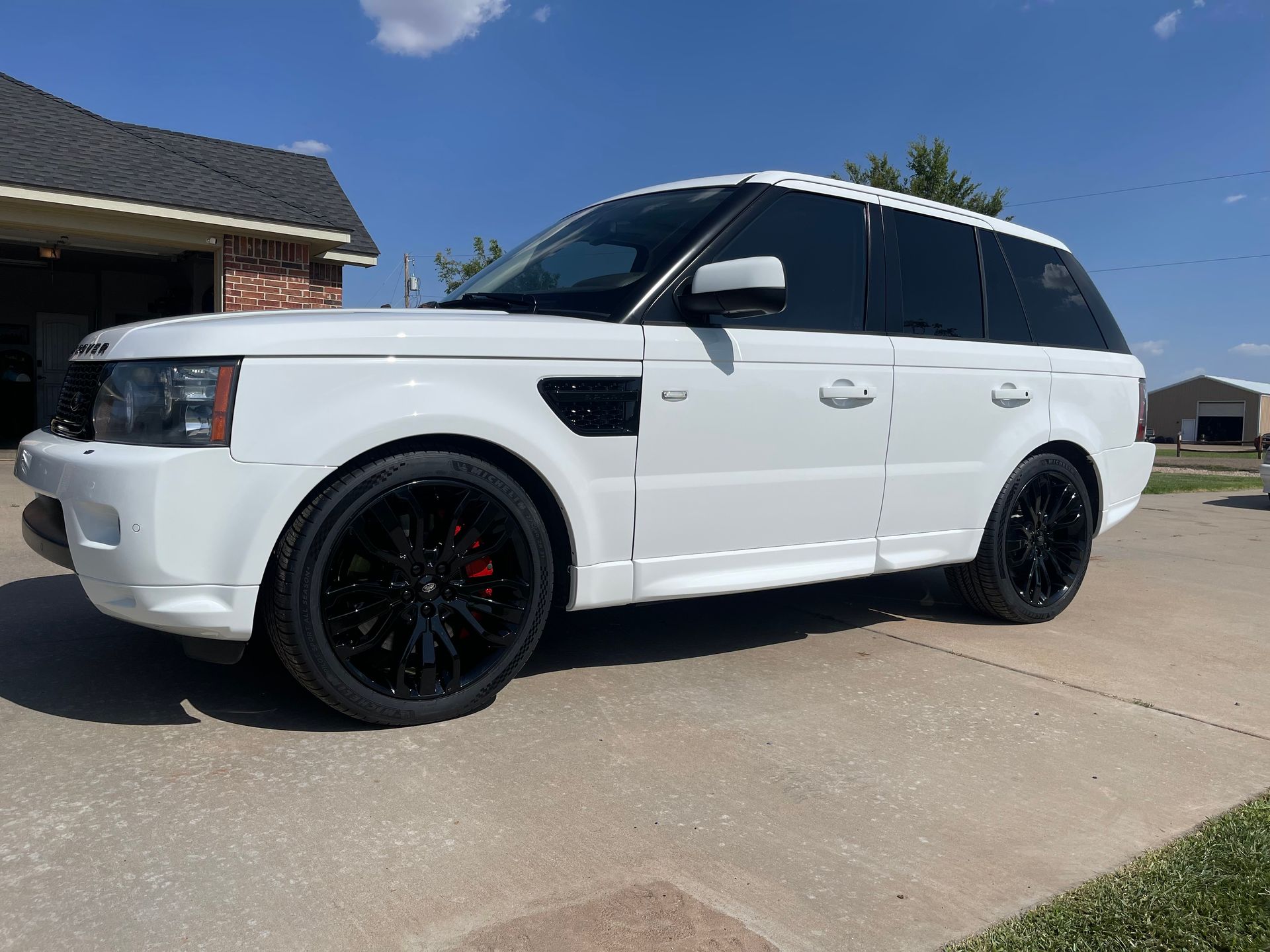 a white range rover sport is parked in a driveway in front of a house .