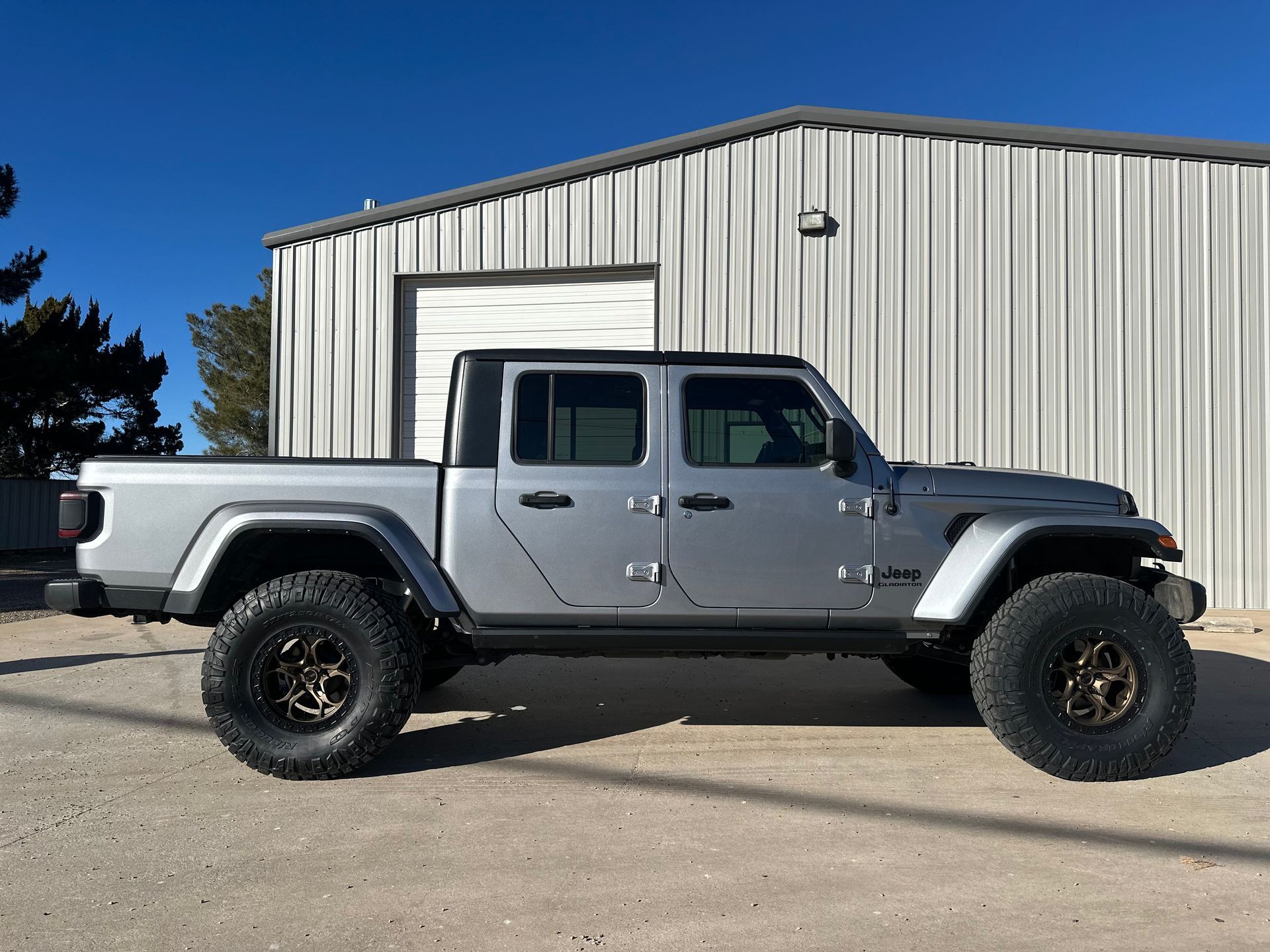 a silver jeep gladiator is parked in front of a building .