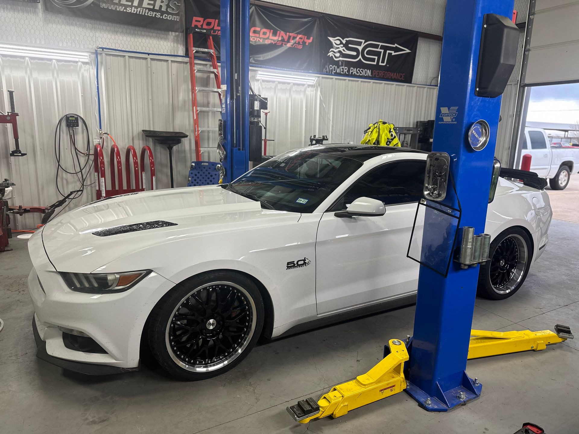 a white mustang is parked on a lift in a garage .