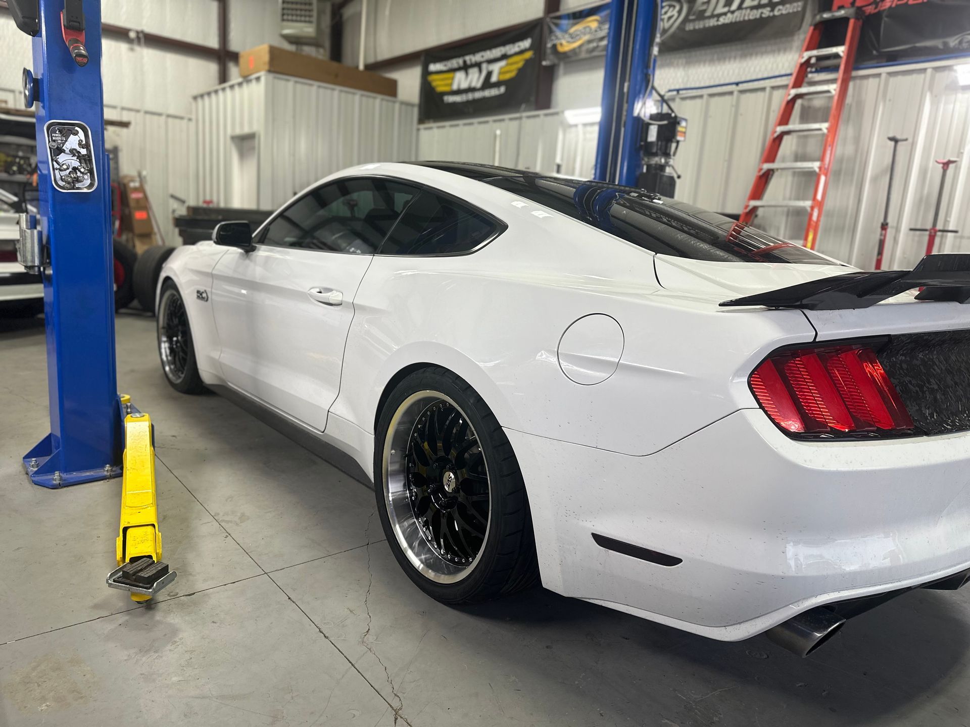 a white mustang is parked on a lift in a garage .