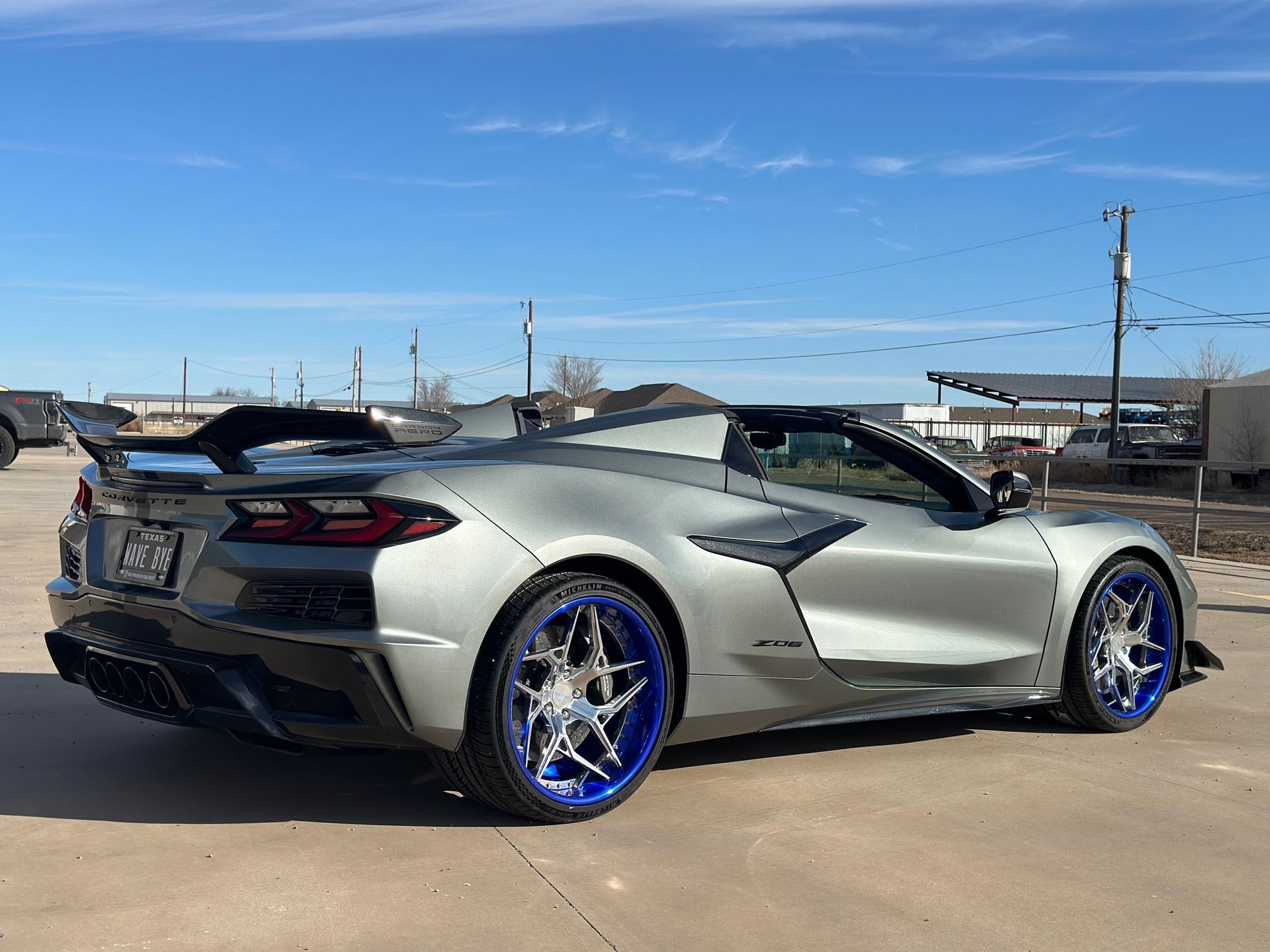 a silver sports car with blue wheels is parked in a parking lot .