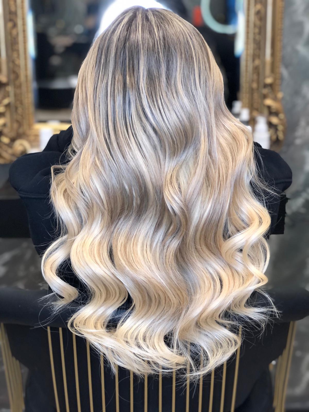 Eine Frau mit langen blonden Haaren sitzt auf einem Stuhl vor einem Spiegel.