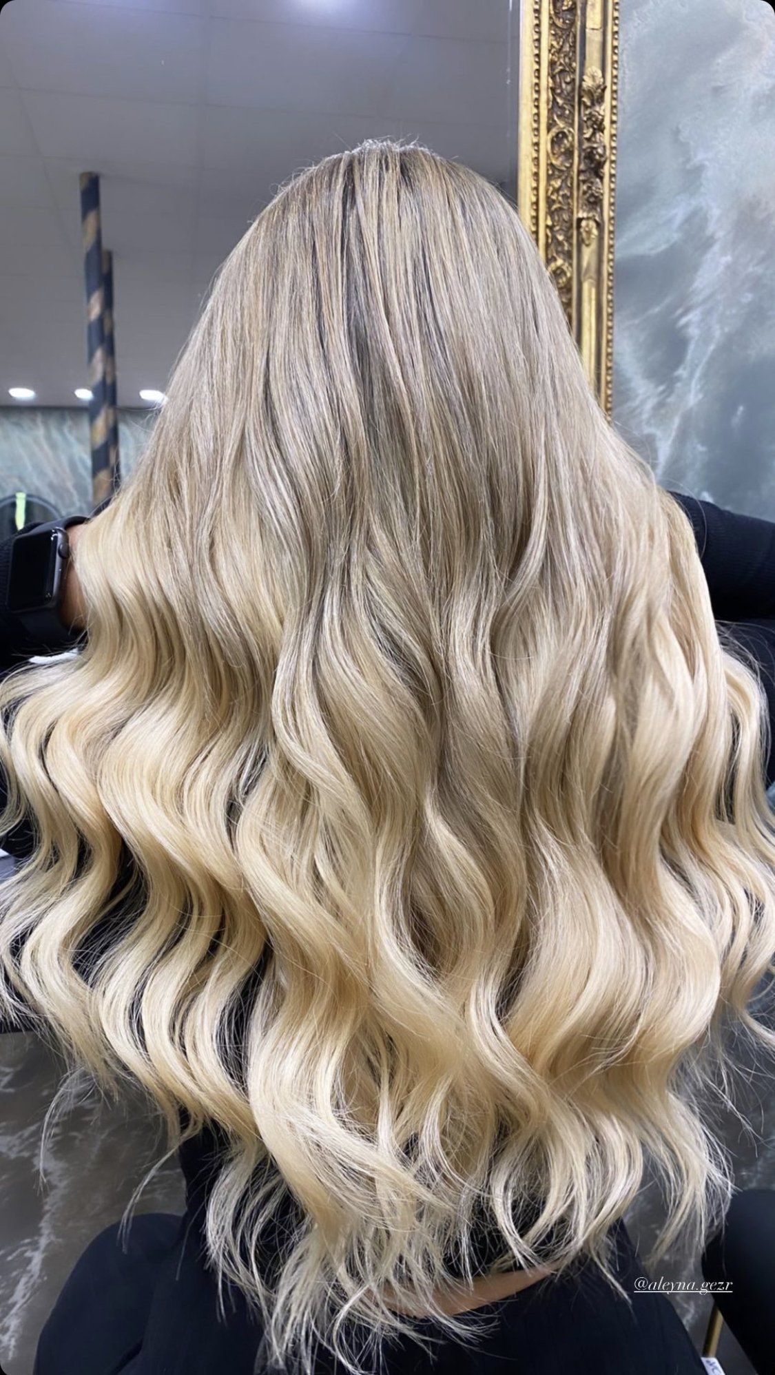 Eine Frau mit blonden Haaren sitzt auf einem Stuhl vor einem Spiegel.