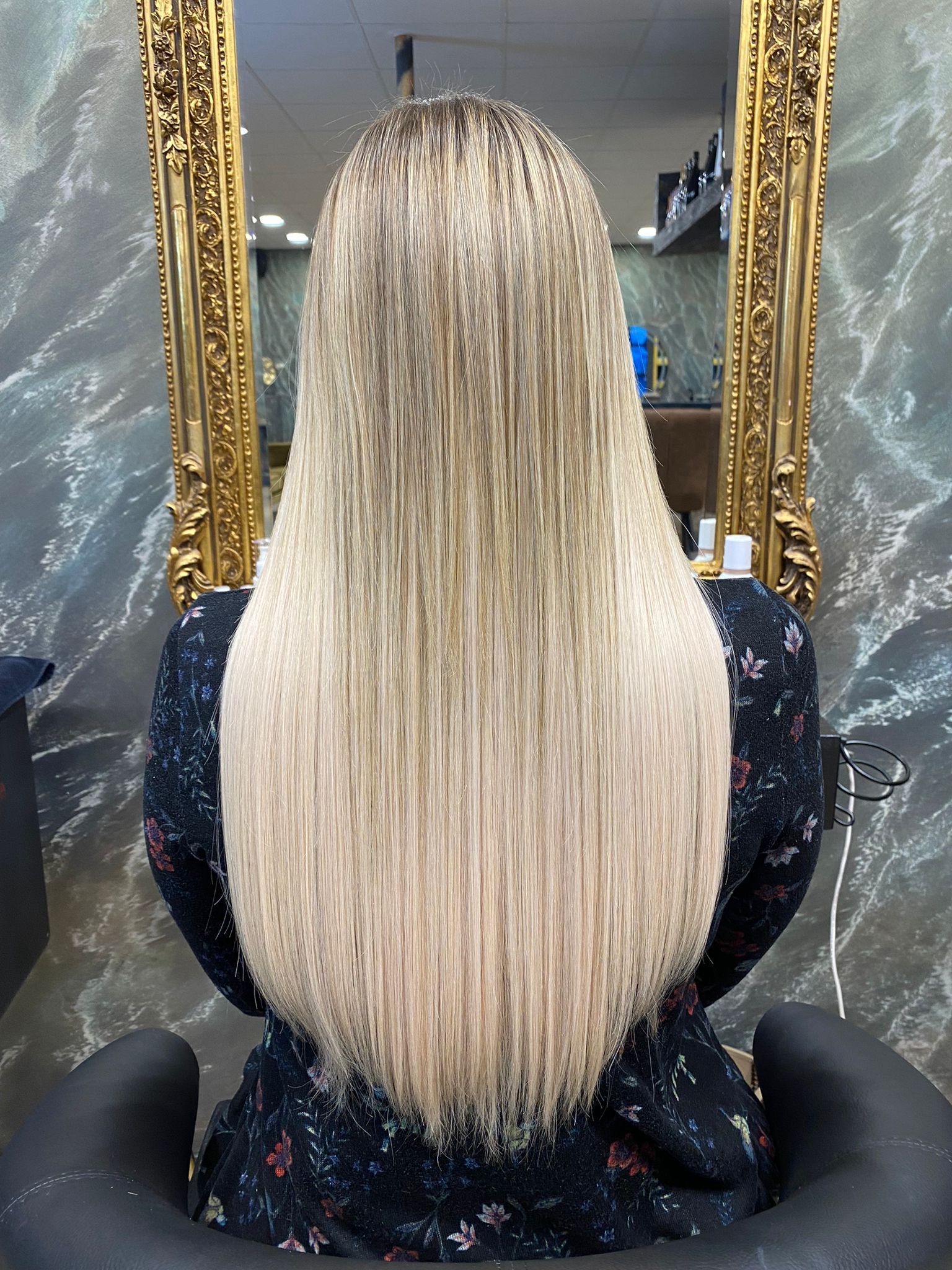 Eine Frau mit langen blonden Haaren sitzt auf einem Stuhl vor einem Spiegel.