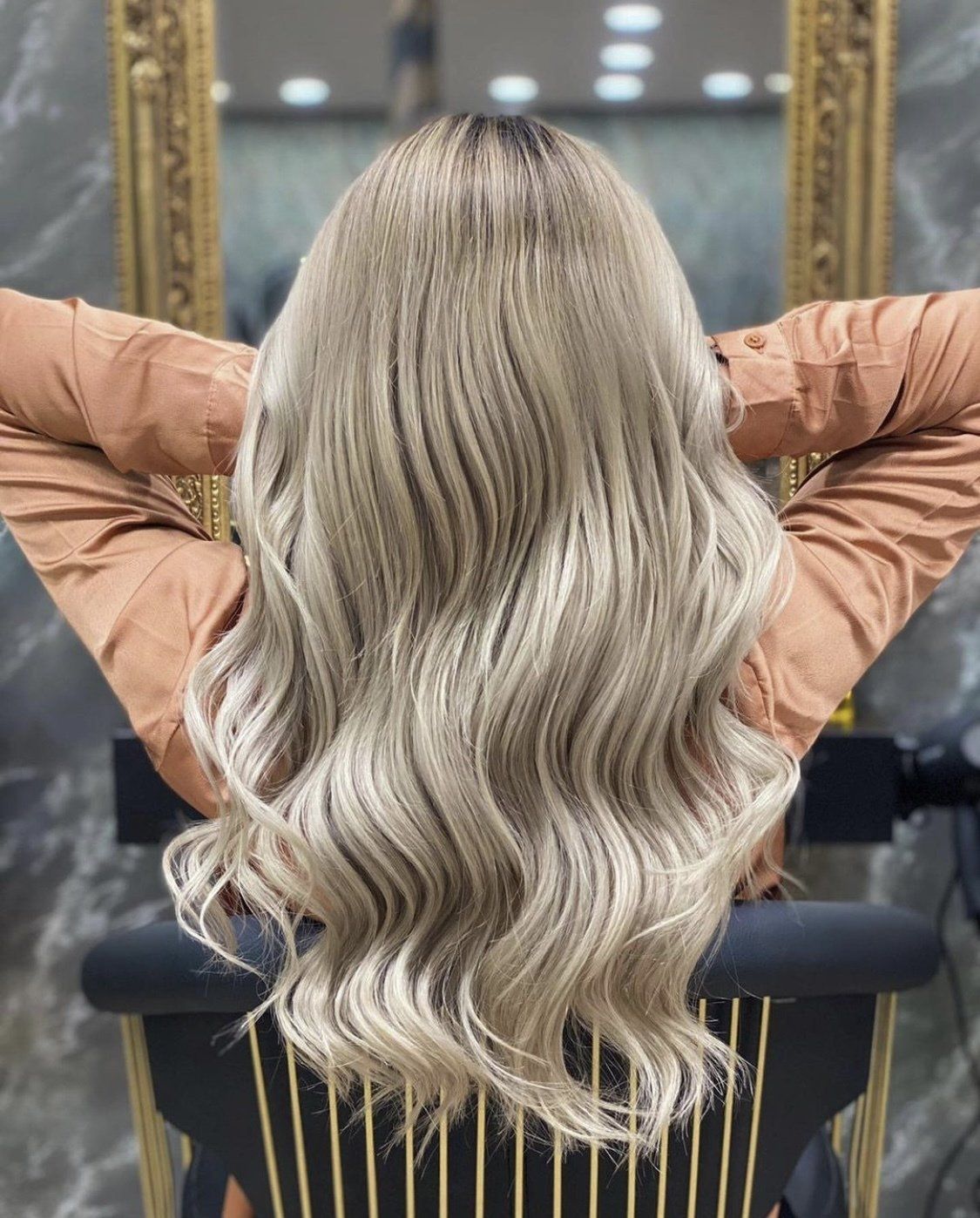 Eine Frau mit langen blonden Haaren sitzt mit den Händen hinter dem Kopf auf einem Stuhl.