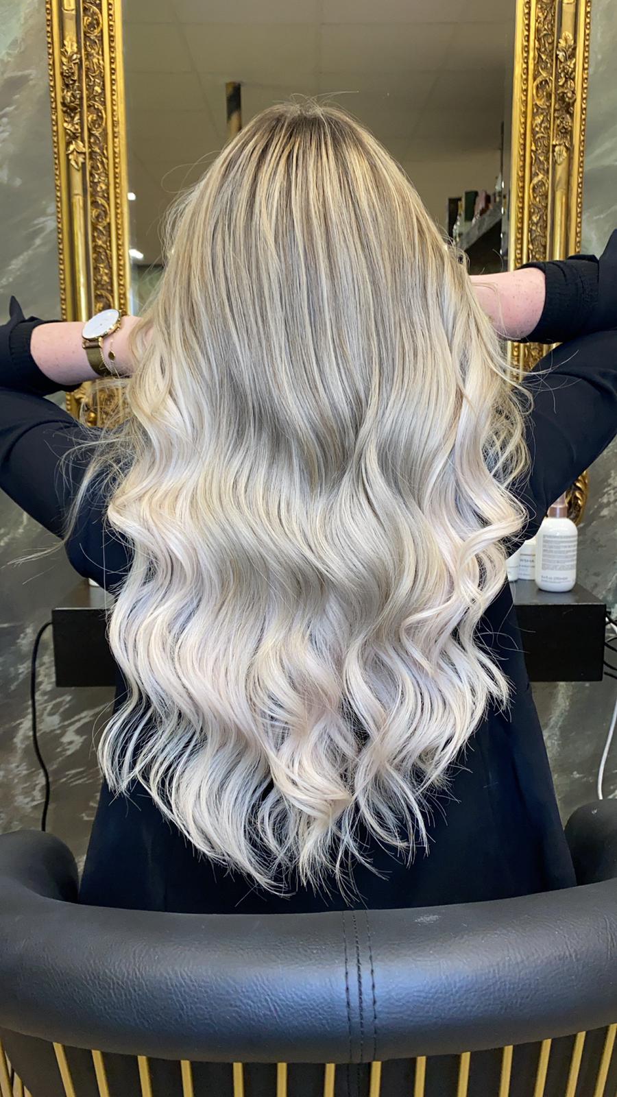 Eine Frau mit langen blonden Haaren sitzt auf einem Stuhl vor einem Spiegel.