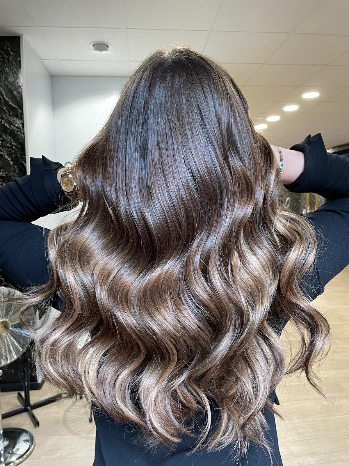 Eine Frau mit langem, welligem, braunem Haar steht in einem Raum und hat ihre Hände im Haar.