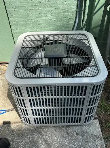 Air conditioning unit, outdoor setting, gray and black metal, square shape, fan visible.