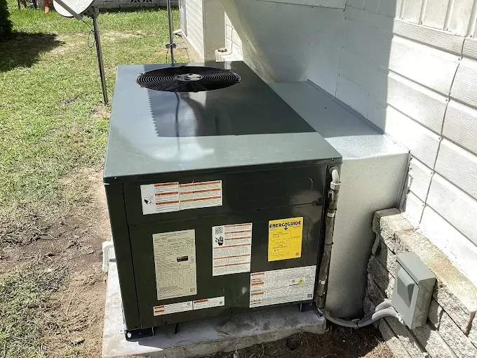 Outdoor air conditioning unit next to a building on a concrete slab.