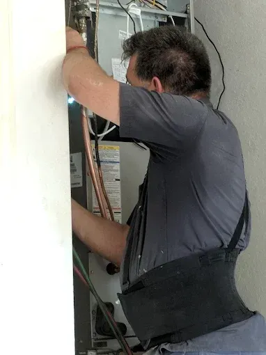 Man working on HVAC system, wearing a back support belt, near a wall.